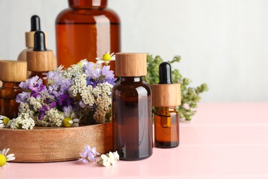 Photo of Aromatherapy. Different essential oils and flowers on pink wooden table, space for text