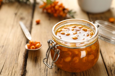 Photo of Delicious sea buckthorn jam and fresh berries on wooden table. Space for text