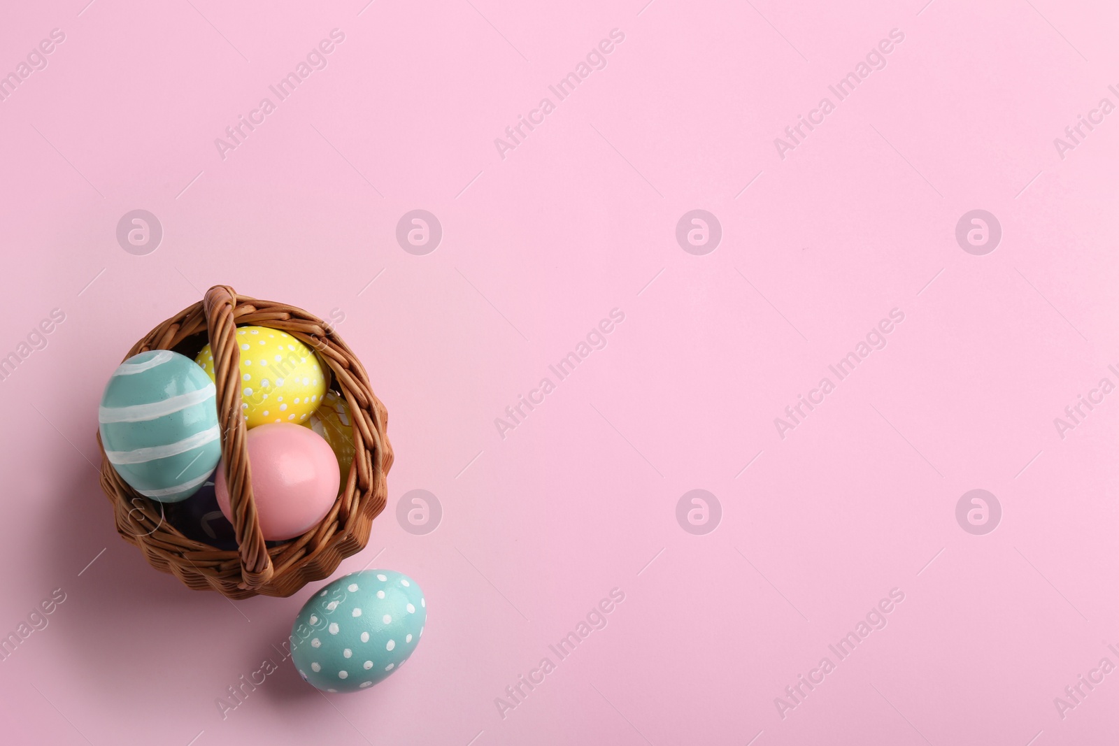 Photo of Wicker basket with painted Easter eggs on color background, top view. Space for text