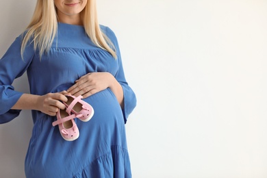 Photo of Pregnant woman holding baby booties near tummy on light background, closeup. Space for text