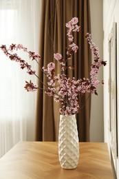 Photo of Blossoming tree twigs in vase on wooden table indoors