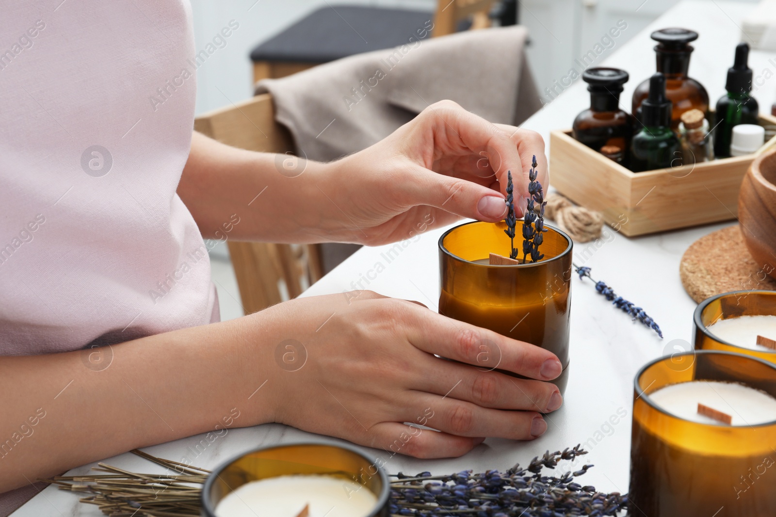 Photo of Woman decorating homemade candle with lavender flowers at table indoors, closeup