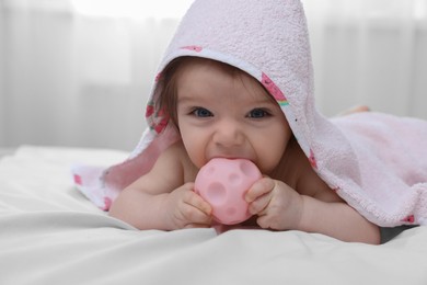 Cute little baby nibbling toy in hooded towel after bathing on bed at home