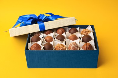 Photo of Box of delicious chocolate candies on yellow background, closeup