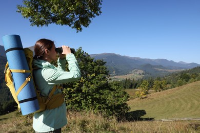 Photo of Tourist with backpack and sleeping pad looking through binoculars in mountains