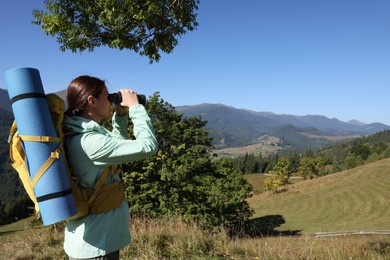 Tourist with backpack and sleeping pad looking through binoculars in mountains