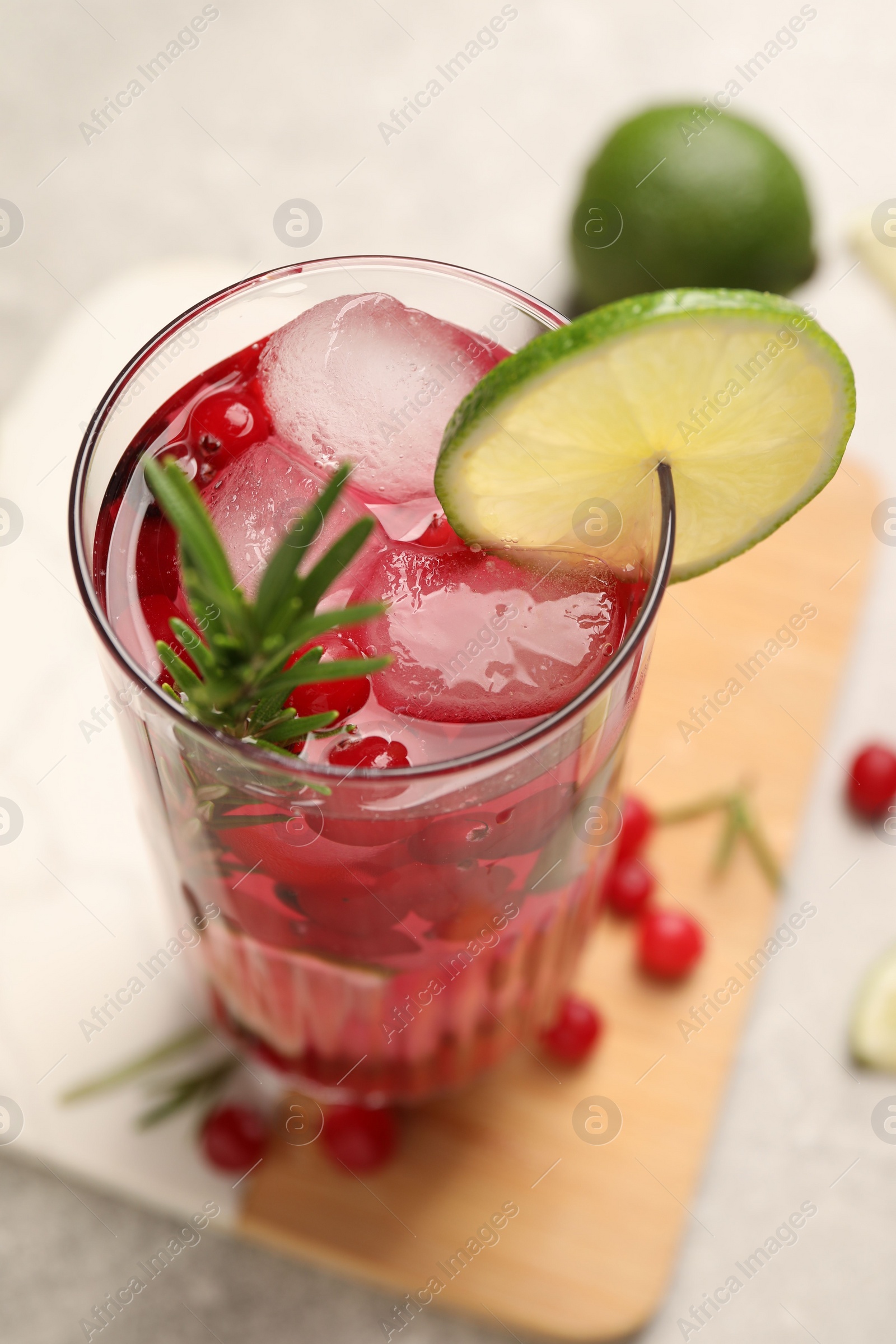 Photo of Tasty cranberry cocktail with rosemary and lime in glass on table, closeup