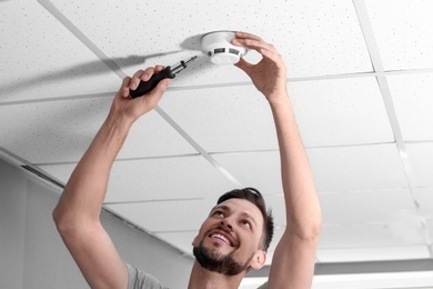 Photo of Male technician installing smoke alarm system indoors