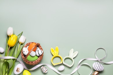 Flat lay composition with Easter eggs in basket and tulip flowers on pale olive background. Space for text
