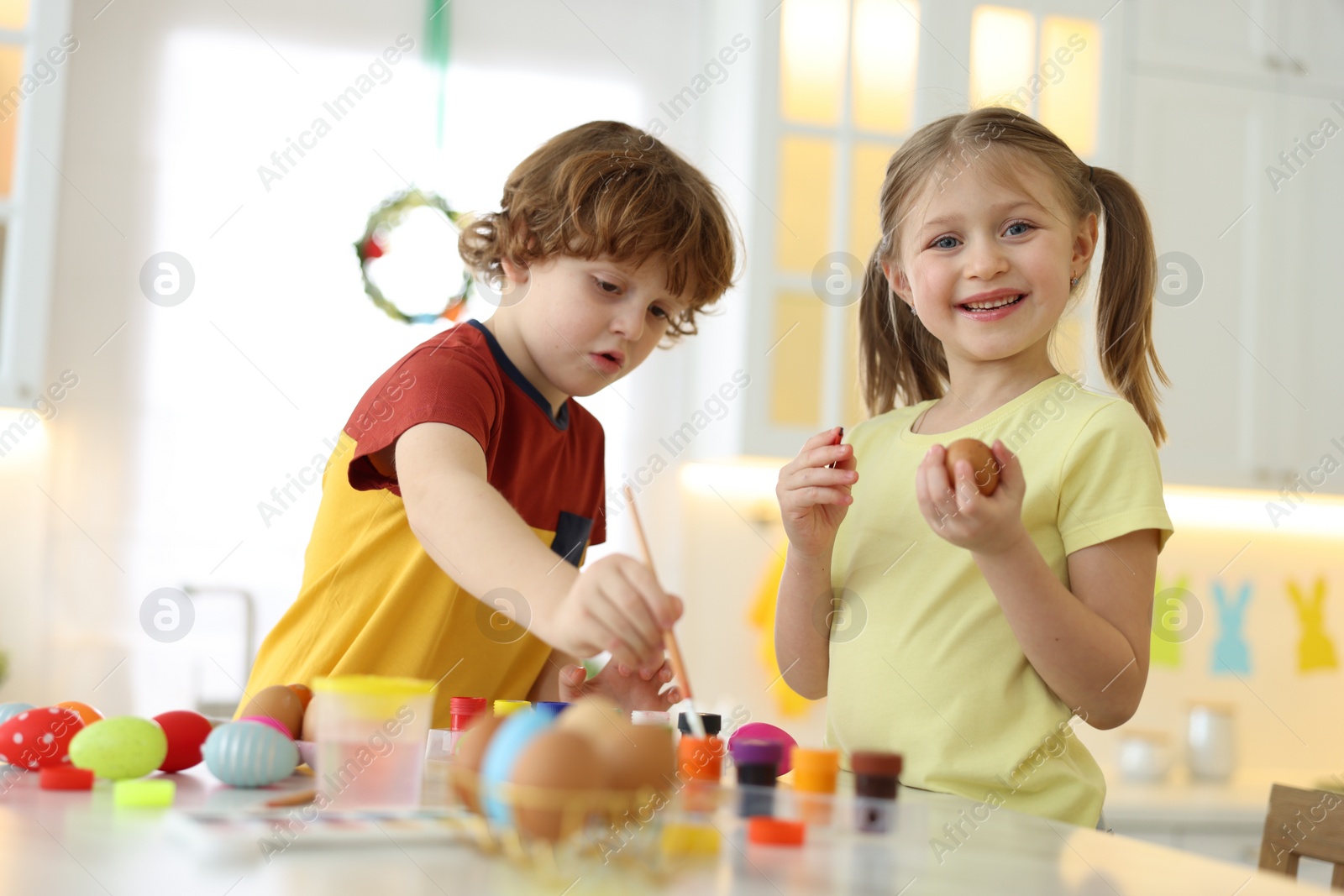 Photo of Easter celebration. Cute children painting eggs at white table in kitchen