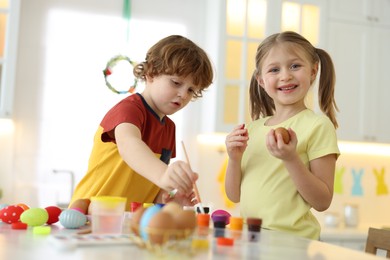 Easter celebration. Cute children painting eggs at white table in kitchen