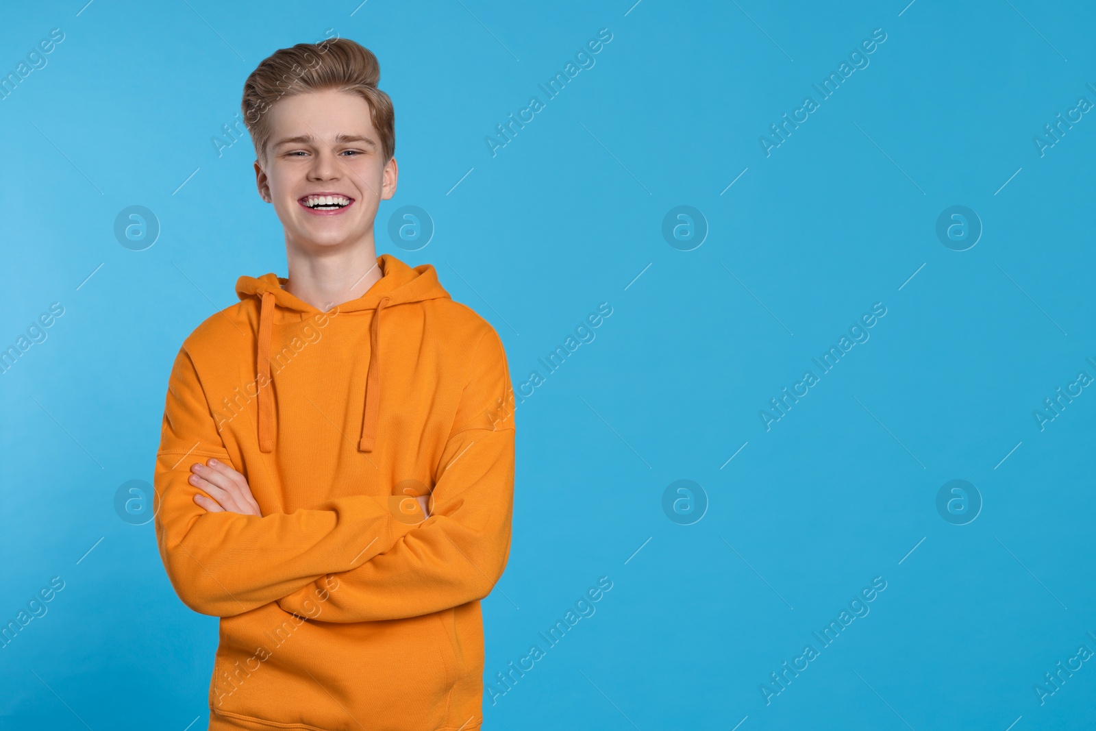 Photo of Portrait of smiling teenage boy on light blue background. Space for text