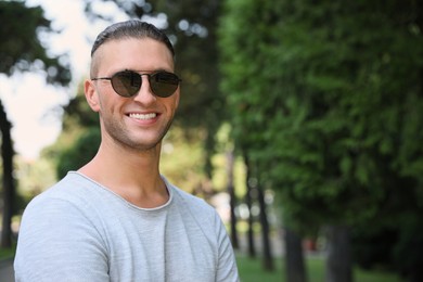 Handsome young man in stylish sunglasses at park, space for text