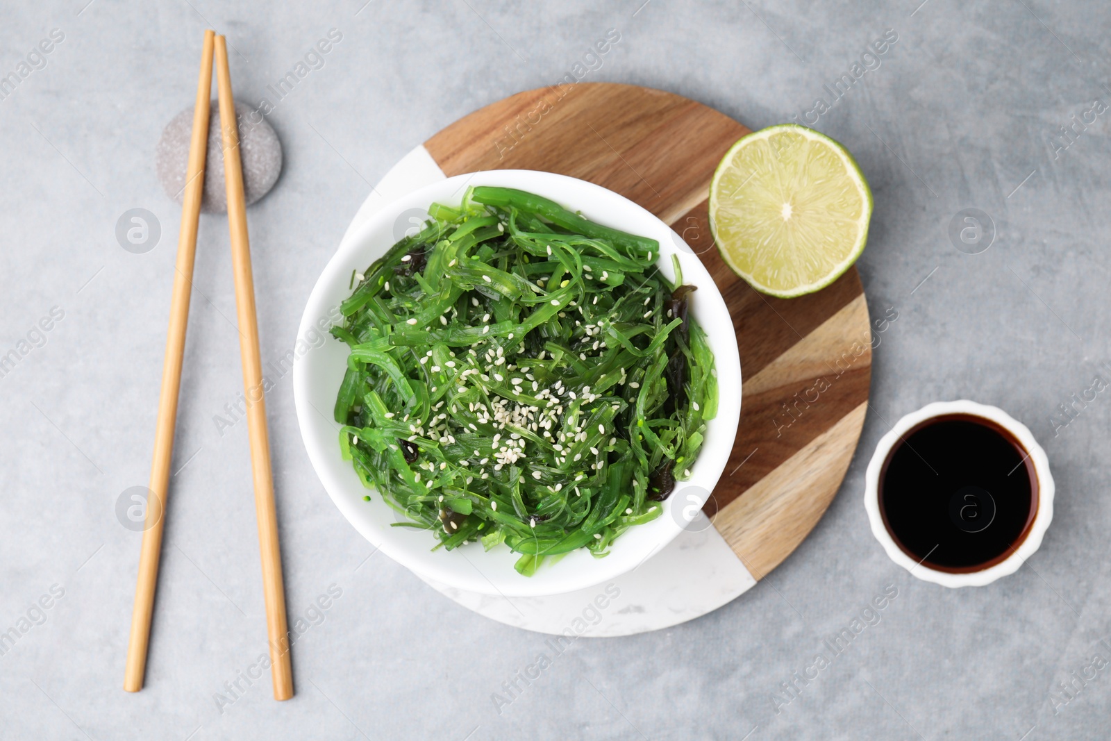 Photo of Tasty seaweed salad in bowl served on gray table, flat lay