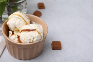 Photo of Scoopsice cream with caramel sauce and candies on light grey table, closeup. Space for text