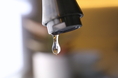 Photo of Water drop falling down from tap on blurred background, closeup