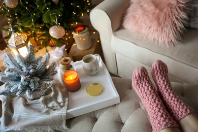 Photo of Woman wearing pink knitted socks in room decorated  for Christmas, closeup