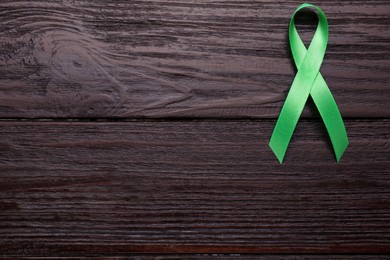 Photo of World Mental Health Day. Green ribbon on wooden background, top view with space for text