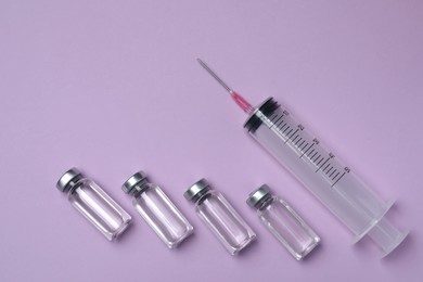 Disposable syringe with needle and vials on violet background, flat lay