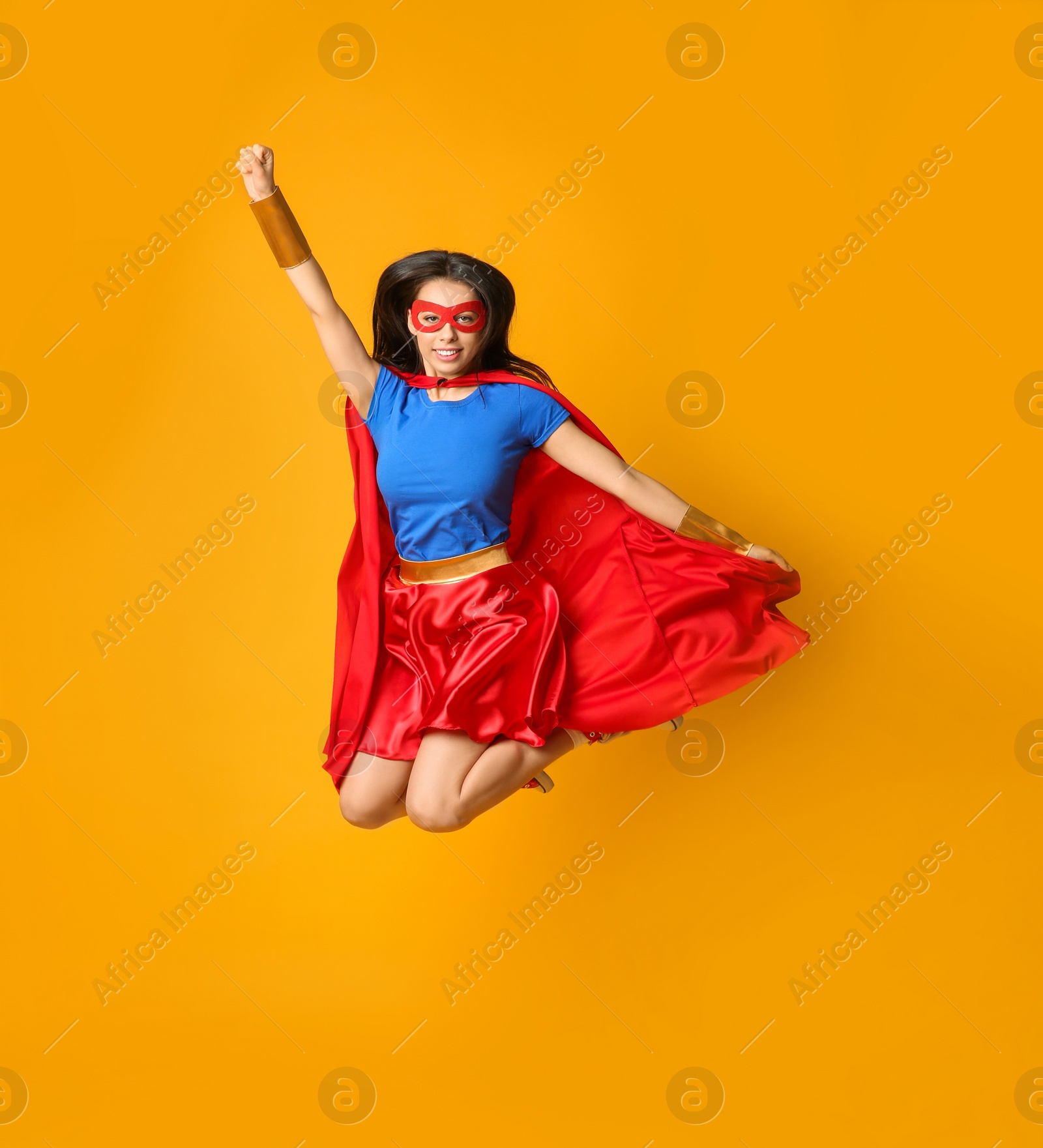Photo of Confident young woman in superhero costume jumping on orange background