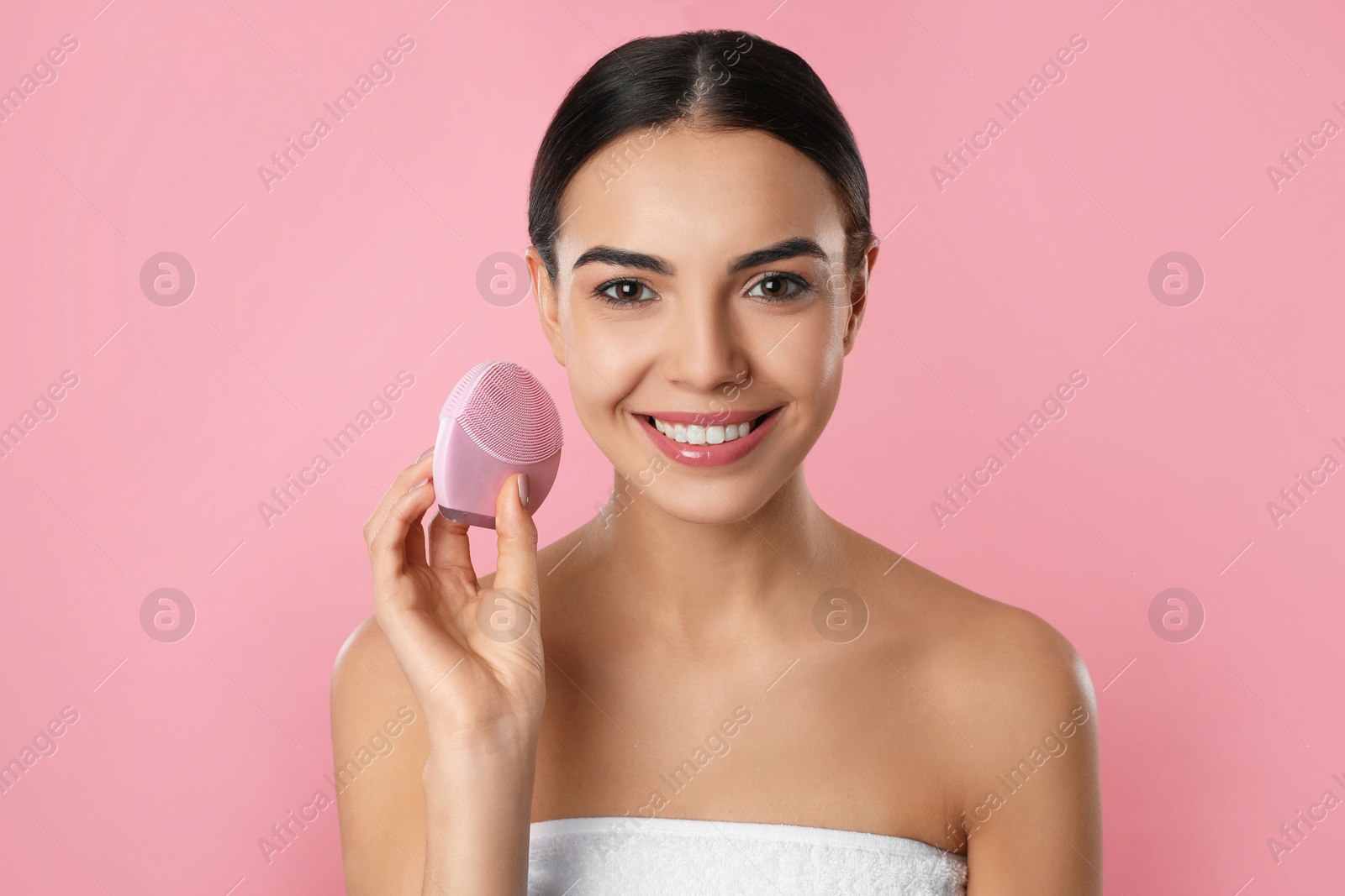 Photo of Young woman holding facial cleansing brush on pink background. Washing accessory
