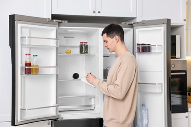 Man writing notes near empty refrigerator in kitchen