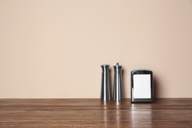 Photo of Napkin holder with salt and pepper shakers on table against color background. Space for text