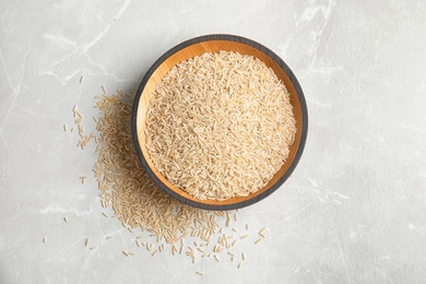 Bowl with raw unpolished rice on light background, top view