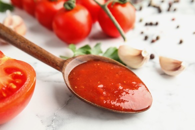 Spoon of tasty tomato sauce on marble table, closeup