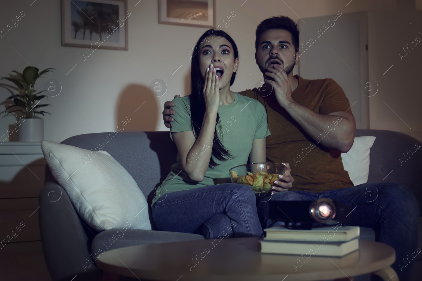 Photo of Emotional young couple watching movie using video projector at home