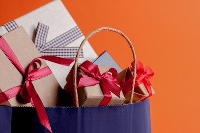 Photo of Dark blue paper shopping bag full of gift boxes on orange background, closeup