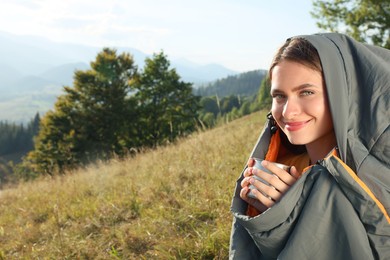 Photo of Young woman with drink in sleeping bag surrounded by beautiful nature
