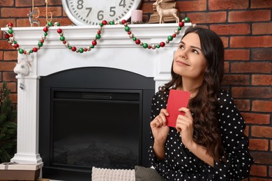 Photo of Young woman with greeting card sitting near fireplace indoors