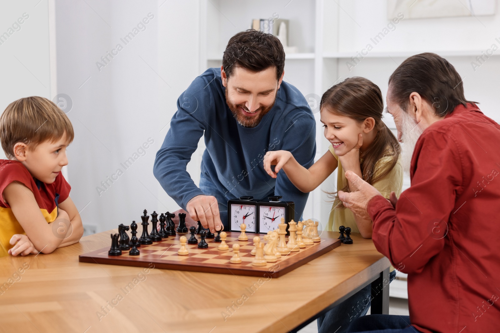 Photo of Family playing chess together at table in room