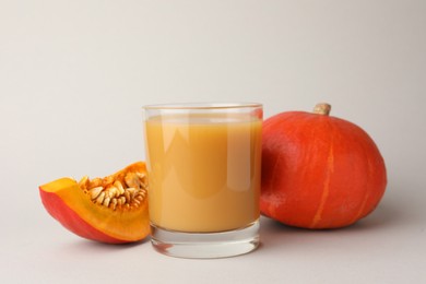 Photo of Tasty pumpkin juice in glass, whole and cut pumpkins on light background