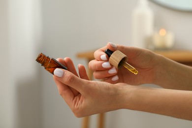 Photo of Young woman applying essential oil on wrist indoors, closeup