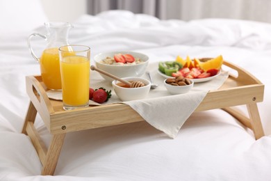 Photo of Tasty breakfast served in bed. Oatmeal, juice, fruits, almonds and honey on wooden tray