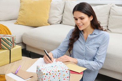 Photo of Young woman writing message in greeting card at table indoors