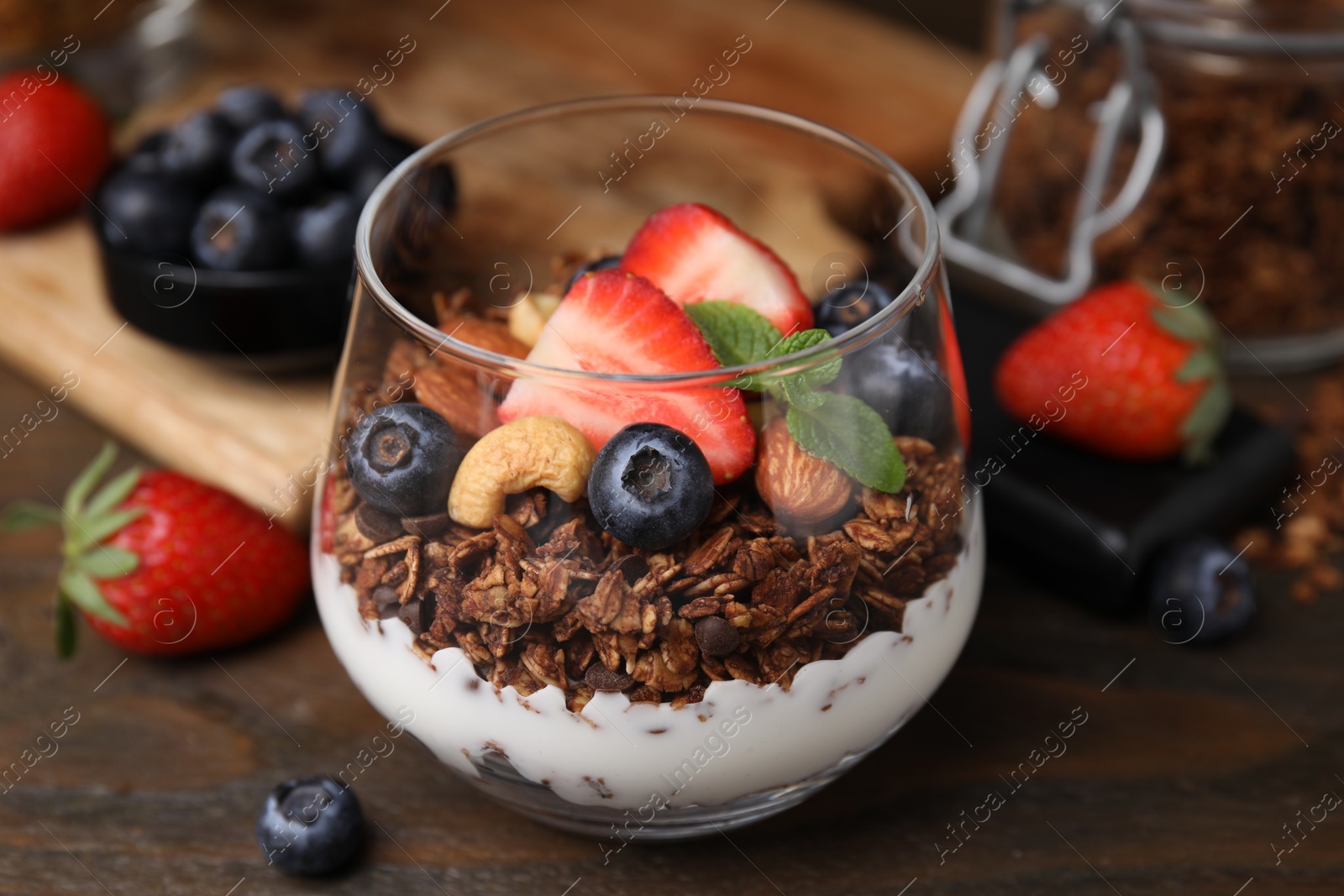 Photo of Tasty granola with berries, nuts and yogurt in glass on wooden table, closeup