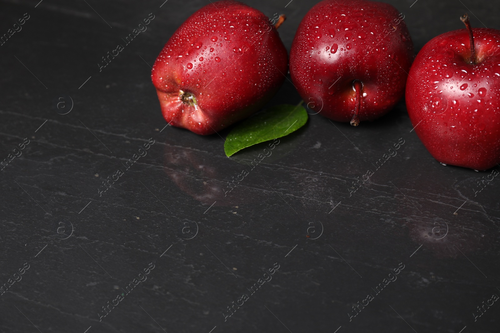 Photo of Wet red apples on dark grey table. Space for text