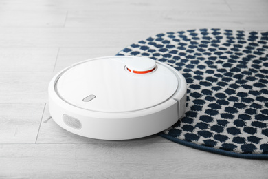 Photo of Hoovering floor with modern robotic vacuum cleaner indoors, closeup