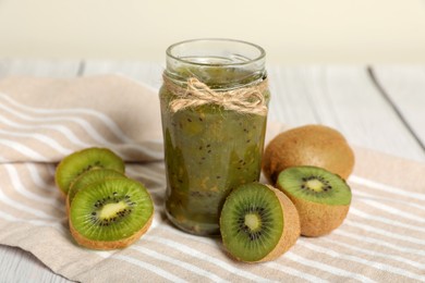 Photo of Jar of delicious kiwi jam and fresh fruits on white wooden table