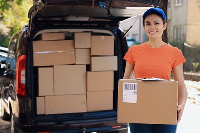 Photo of Courier holding package near delivery truck outdoors