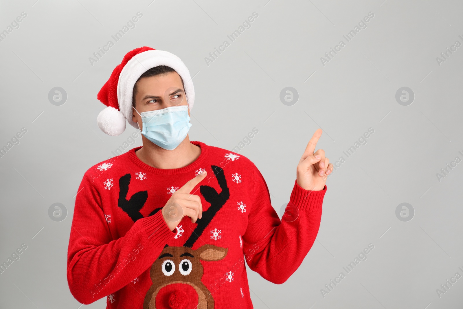 Photo of Man wearing Santa hat and medical mask on grey background