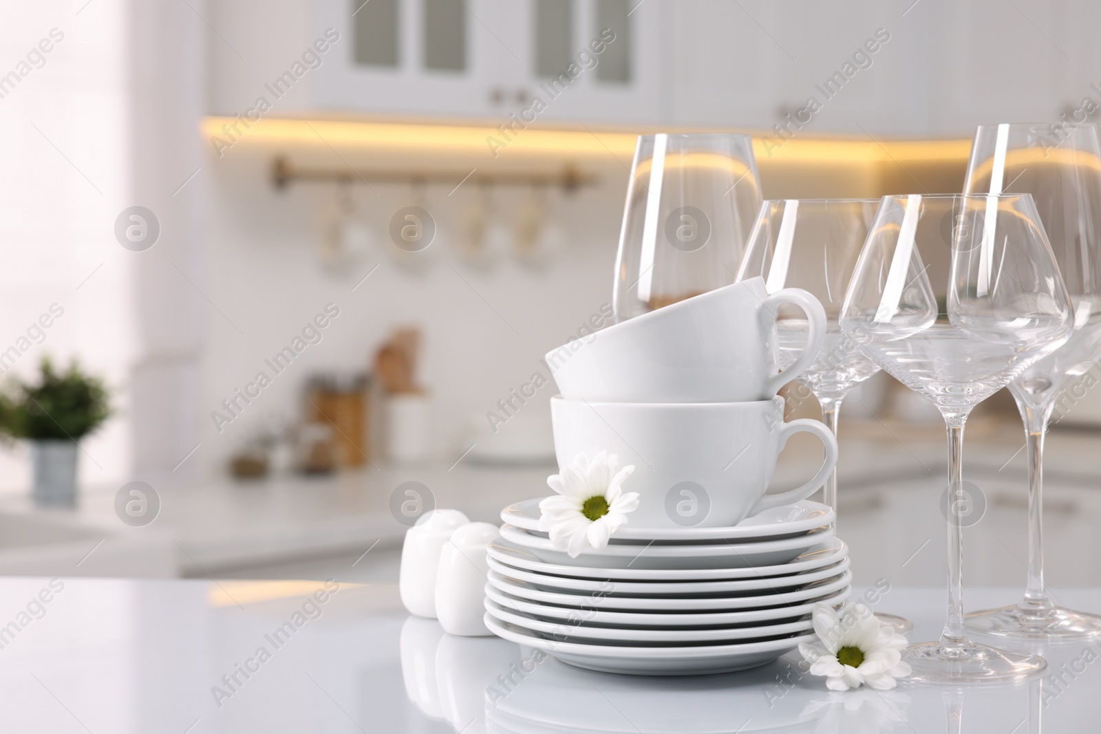 Photo of Set of clean dishware, glasses and flowers on table in kitchen, space for text