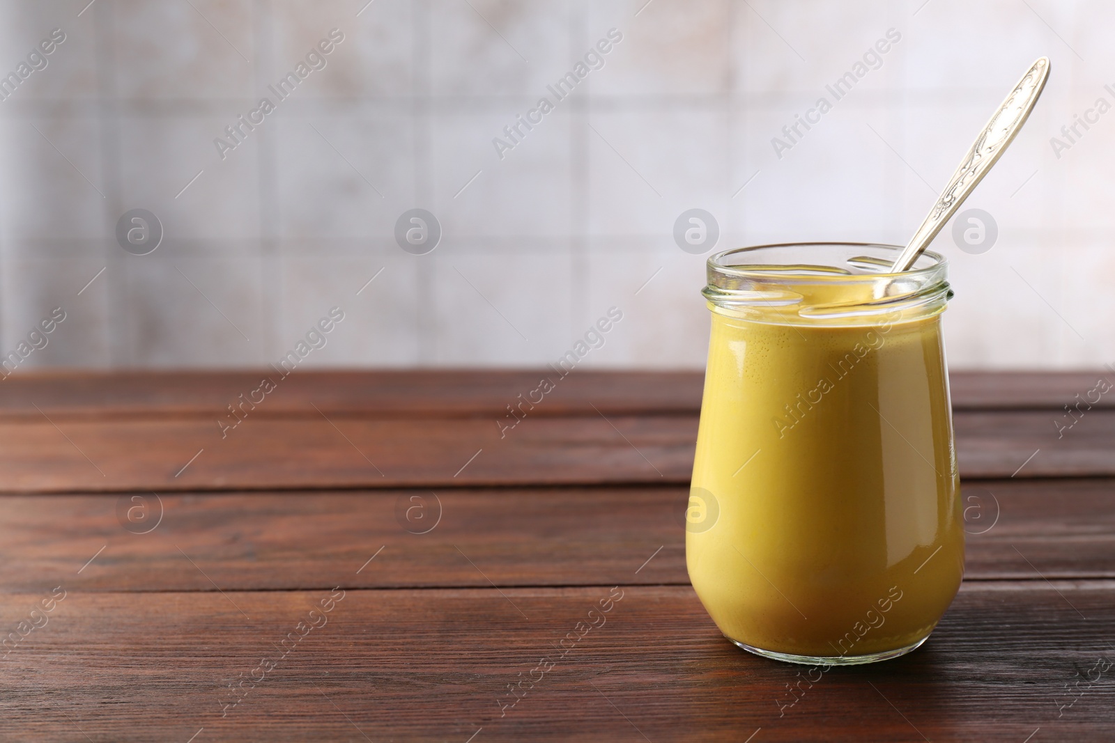 Photo of Tasty mustard sauce and spoon in glass jar on wooden table, space for text