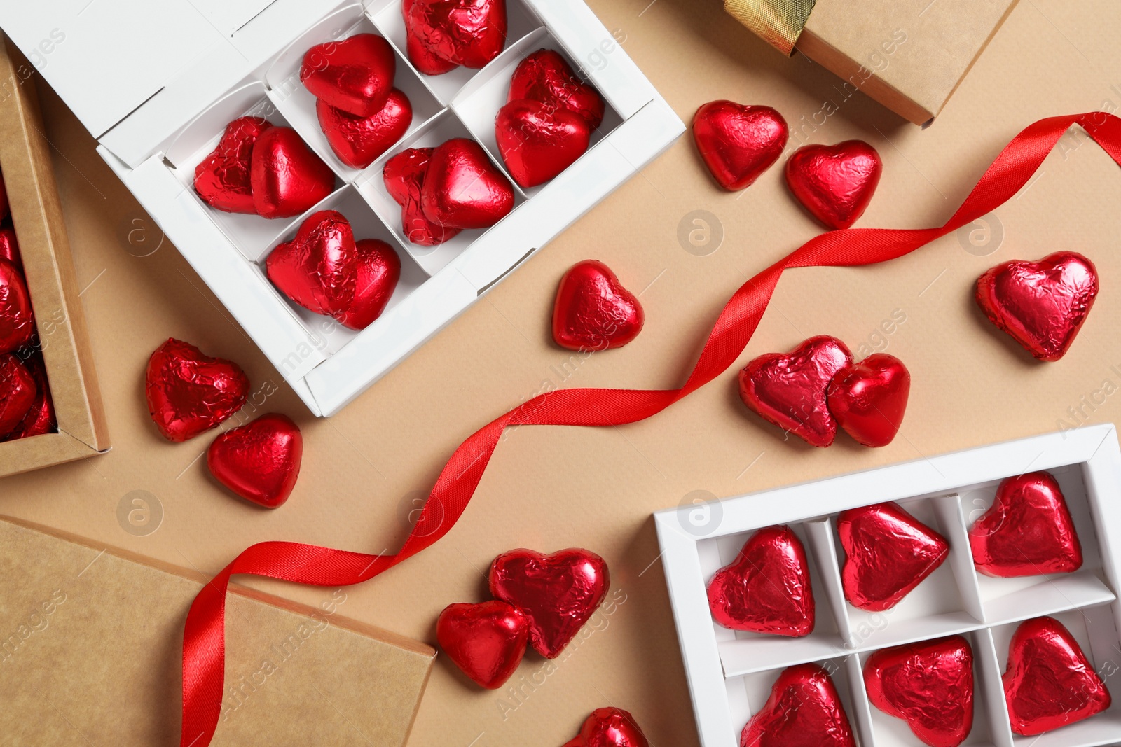 Photo of Beautiful heart shaped chocolate candies in boxes on beige background, flat lay