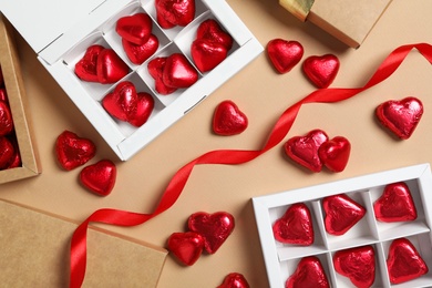 Beautiful heart shaped chocolate candies in boxes on beige background, flat lay