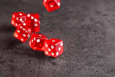 Photo of Many red game dices falling on grey textured table. Space for text