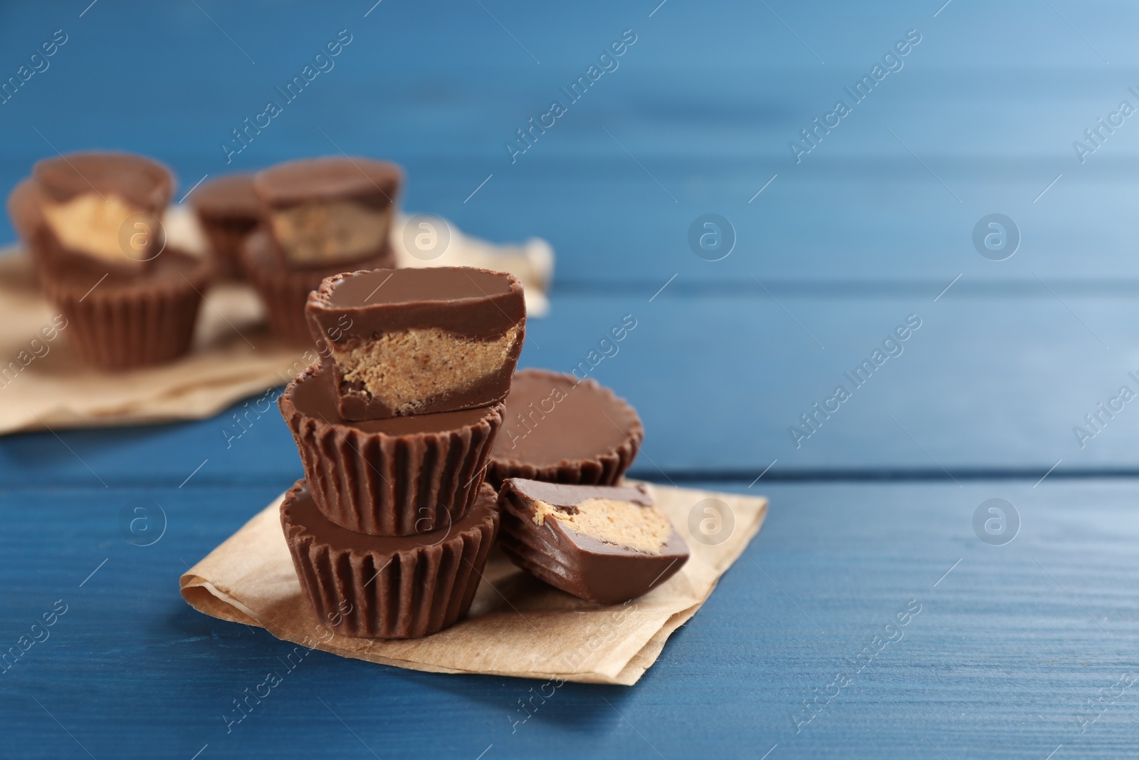 Photo of Cut and whole delicious peanut butter cups on blue wooden table, space for text